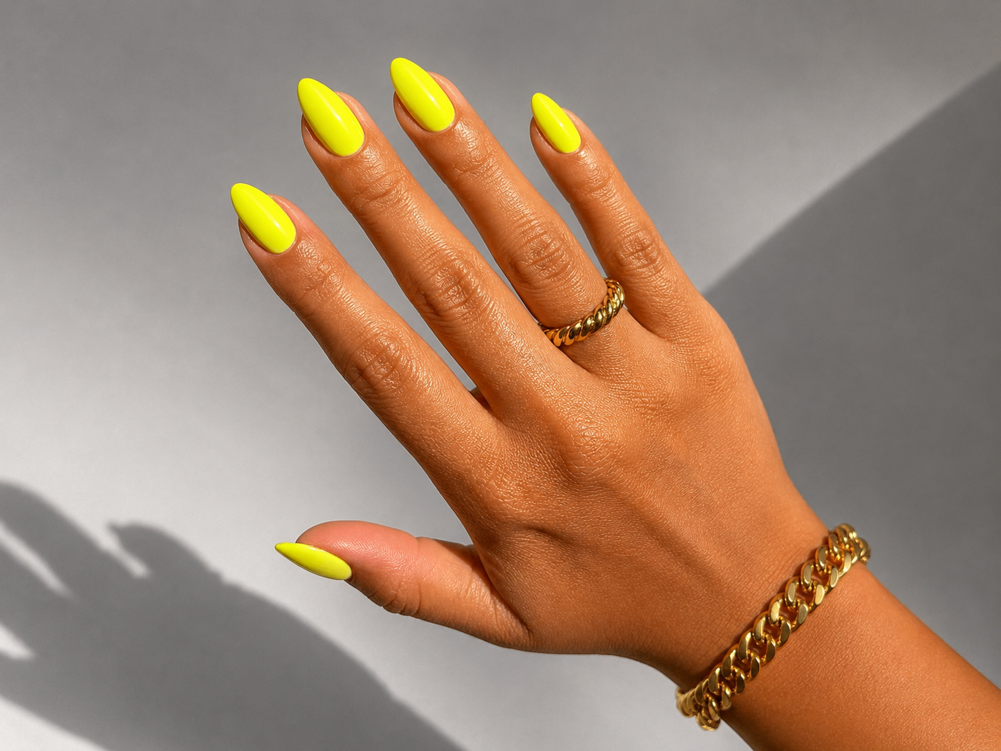 Close-up of vivid neon yellow gel manicure with almond-shaped nails and gold rings