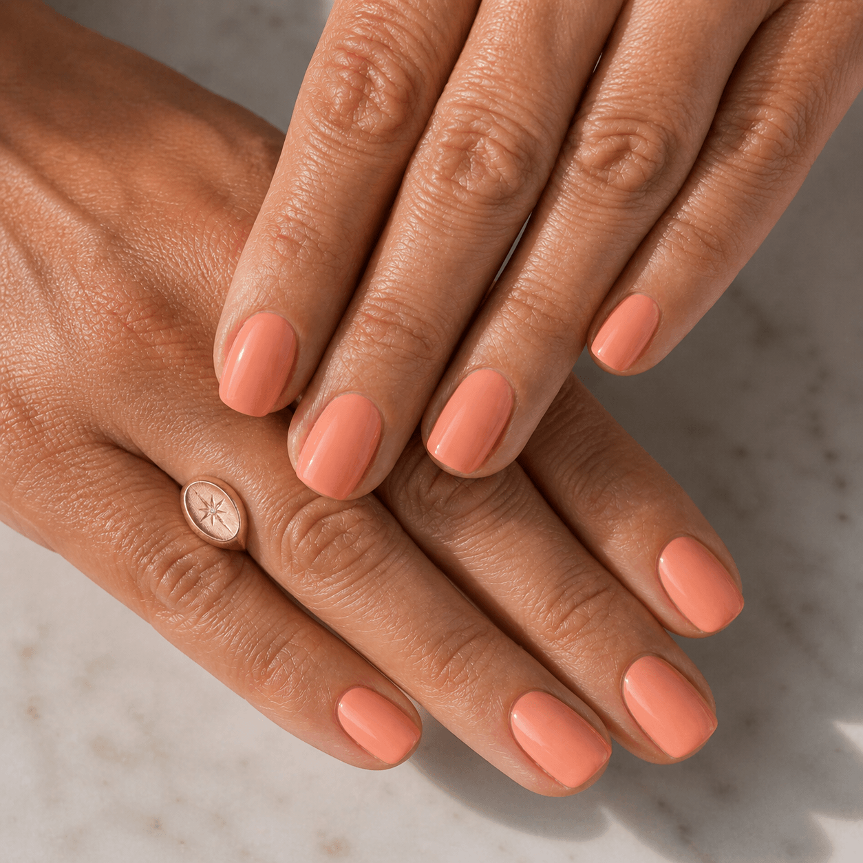 Close-up of mature hands with short squoval nails in creamy warm coral gel, glossy finish in natural daylight