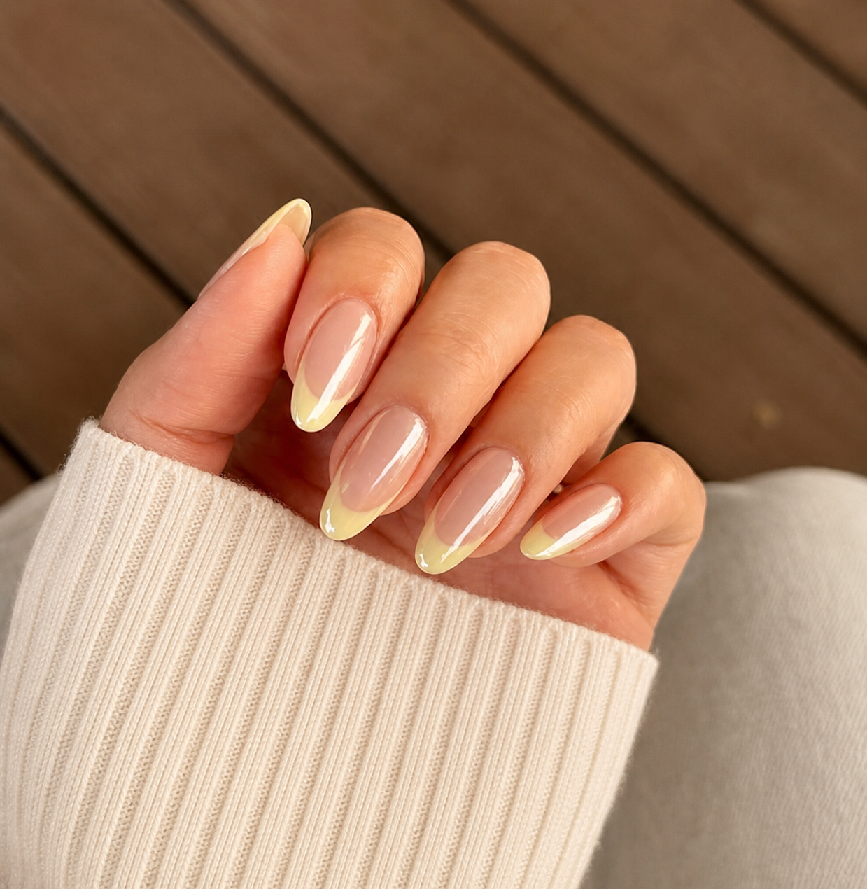 Natural nude nails with soft yellow French tips styled against a warm knit sleeve
