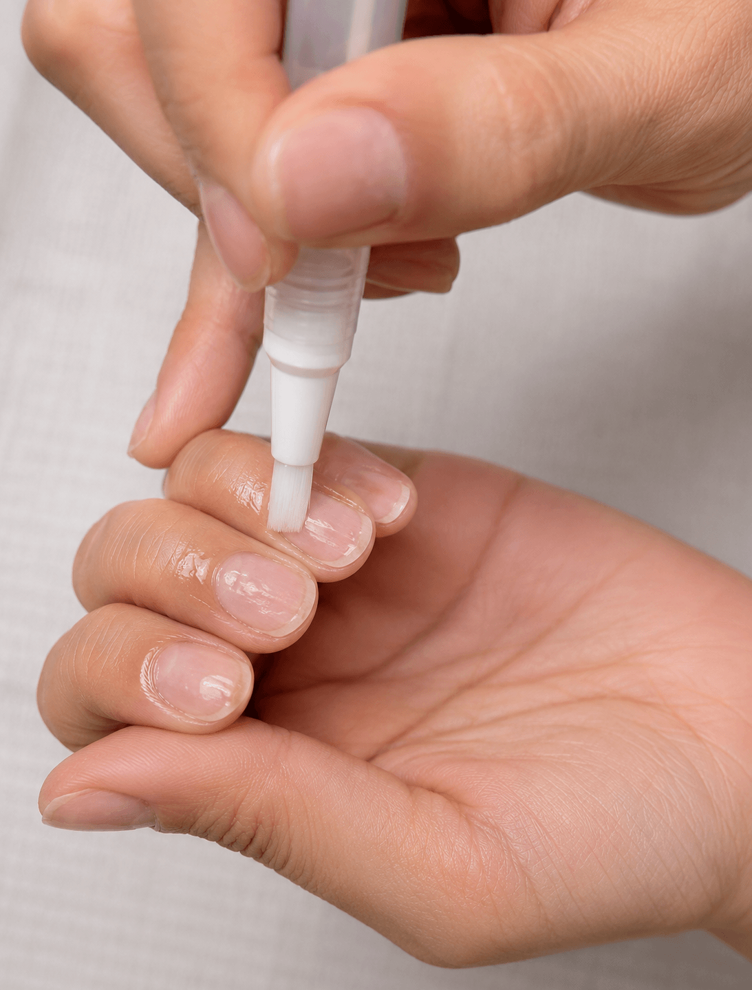Applying cuticle oil to clean natural nails after acrylic nail removal to hydrate and nourish the nails and surrounding skin