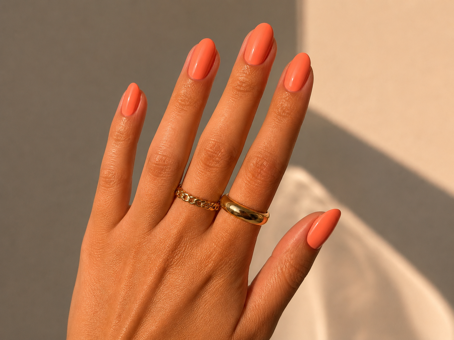 Coral peach almond nails with gold rings in warm natural sunlight