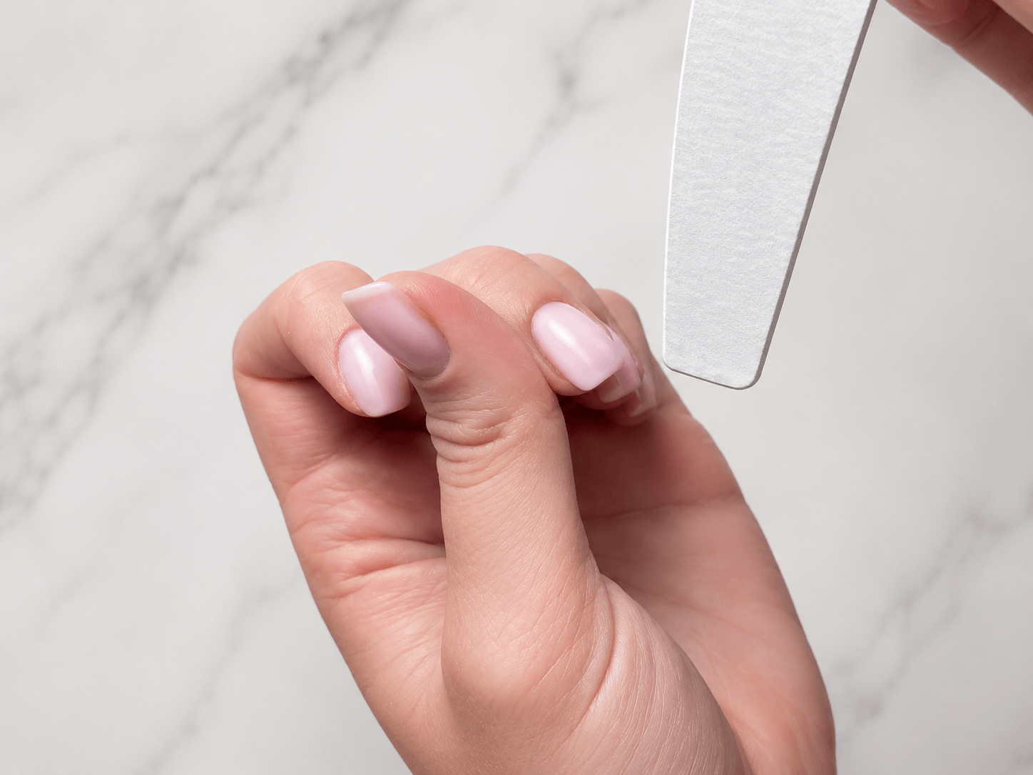 Close-up of filing BIAB builder gel nails with a white nail file before removal