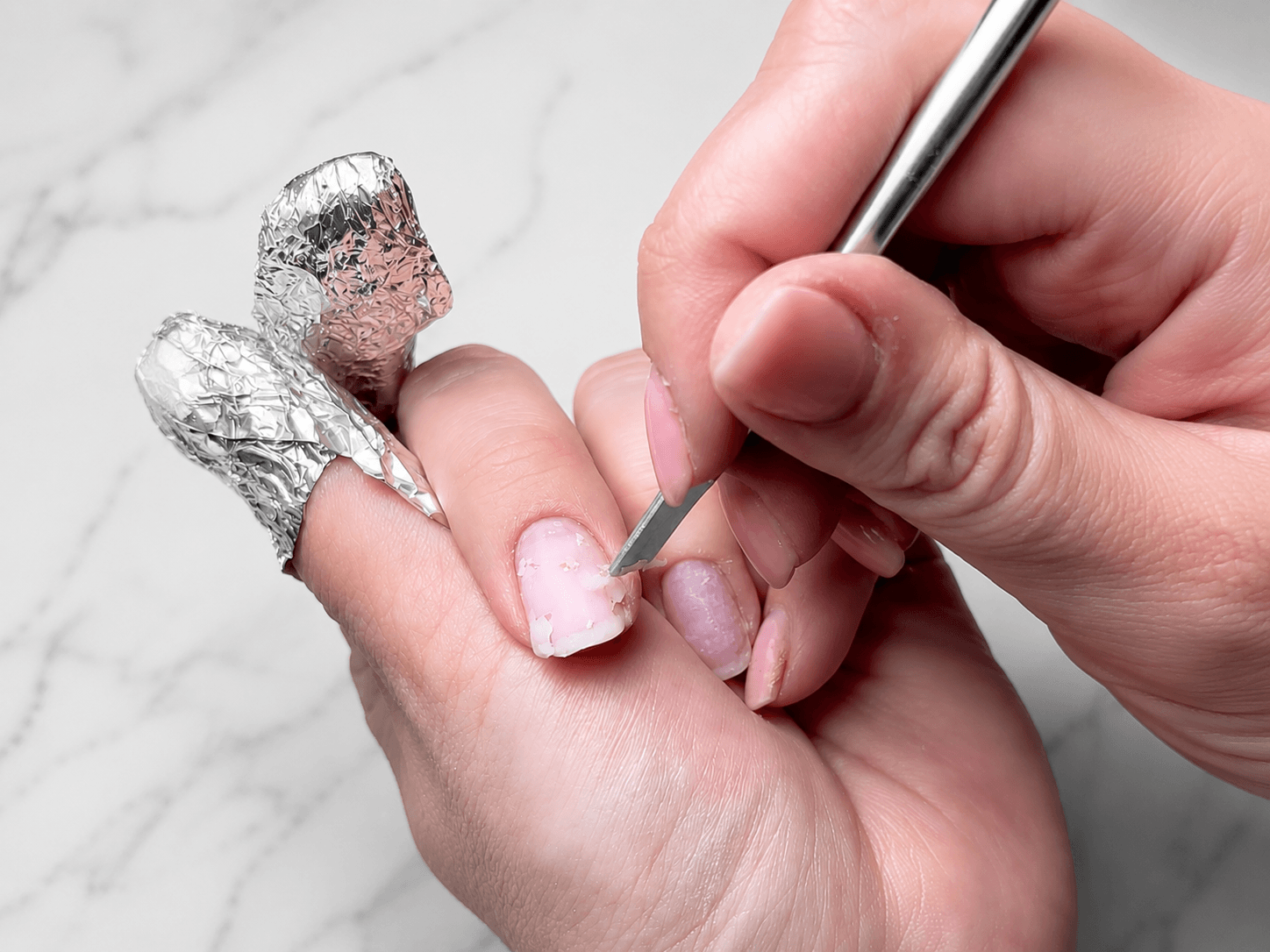 Close-up of cuticle pusher removing soaked BIAB builder gel from natural nails