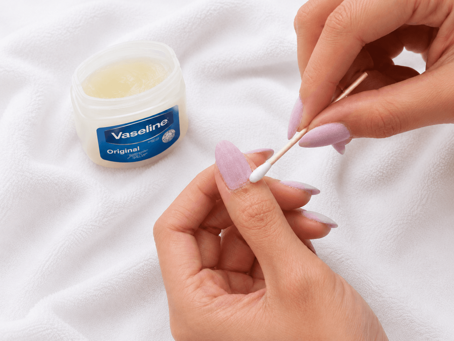 Close-up of applying Vaseline petroleum jelly to cuticles with a cotton swab to protect skin before BIAB removal