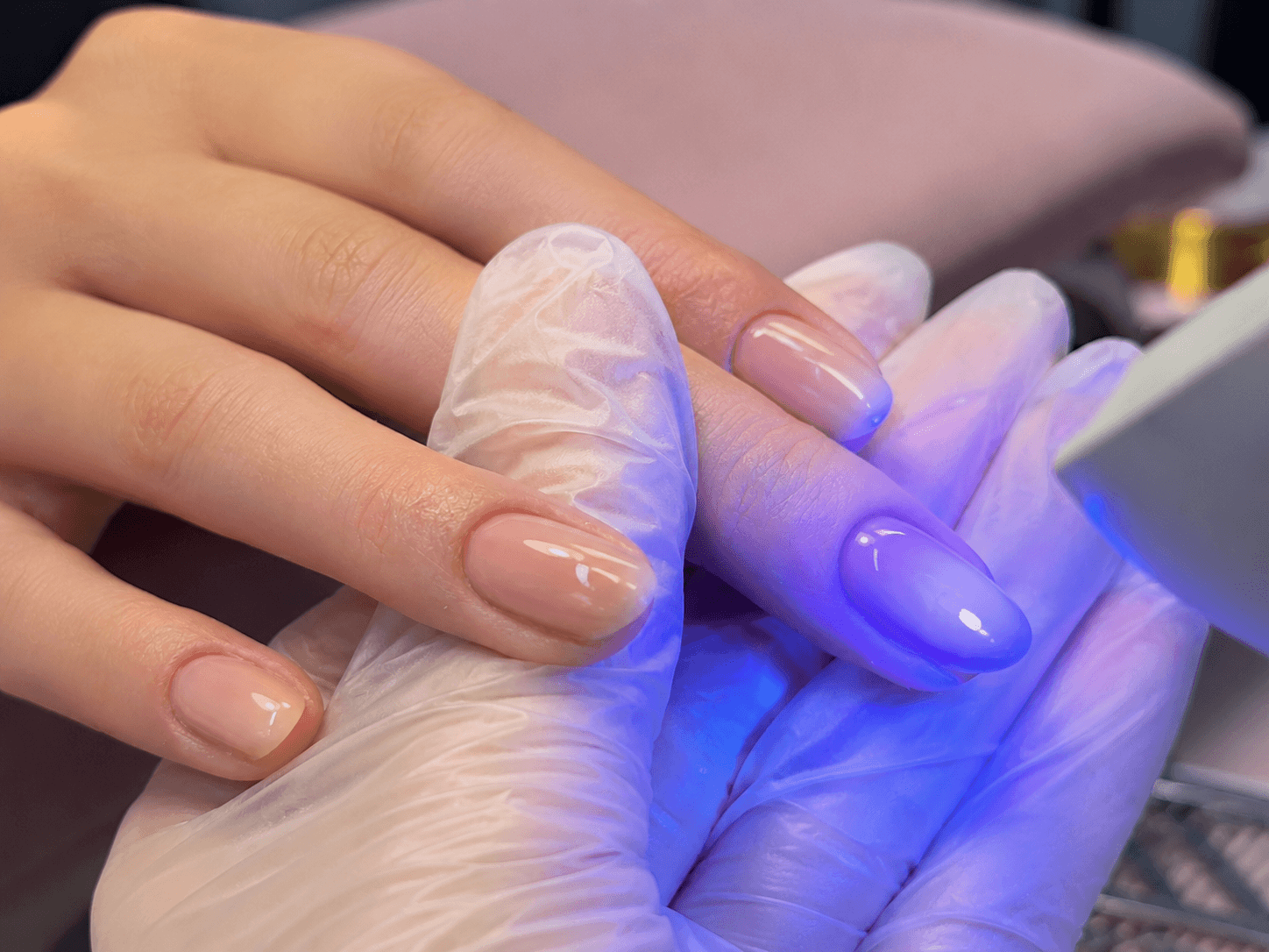 Close-up of BIAB builder gel nails being cured under a UV LED lamp in a nail salon