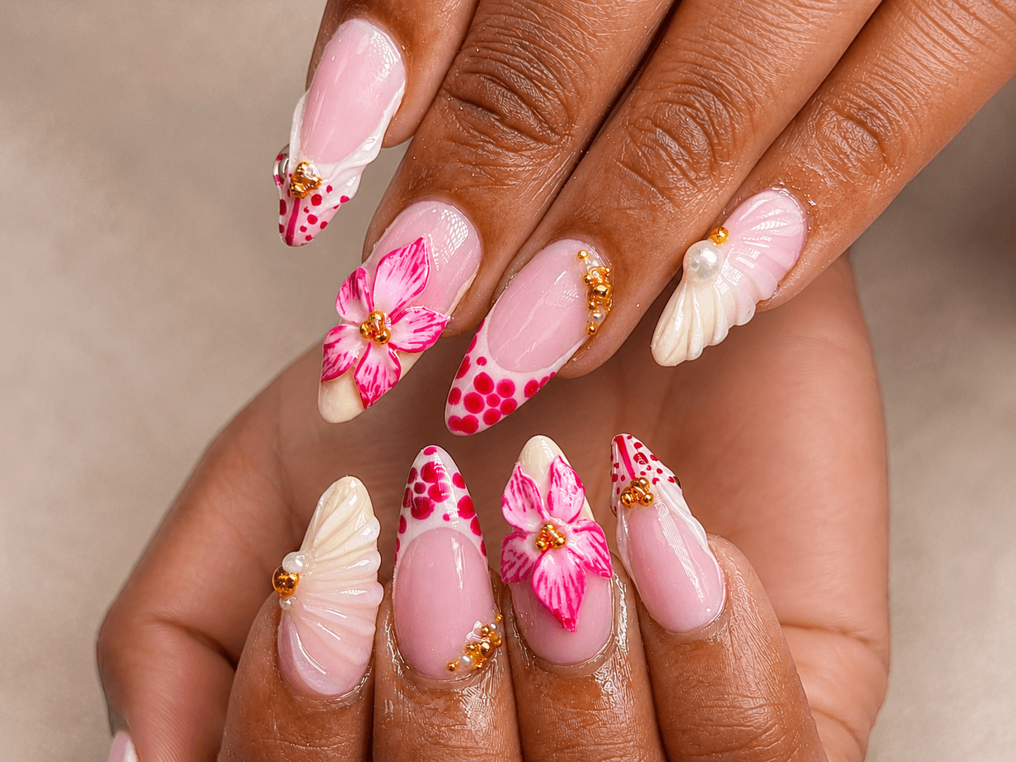 Pink floral 3D nail art with shell accents, gold embellishments and glossy almond-shaped nails in a close-up view