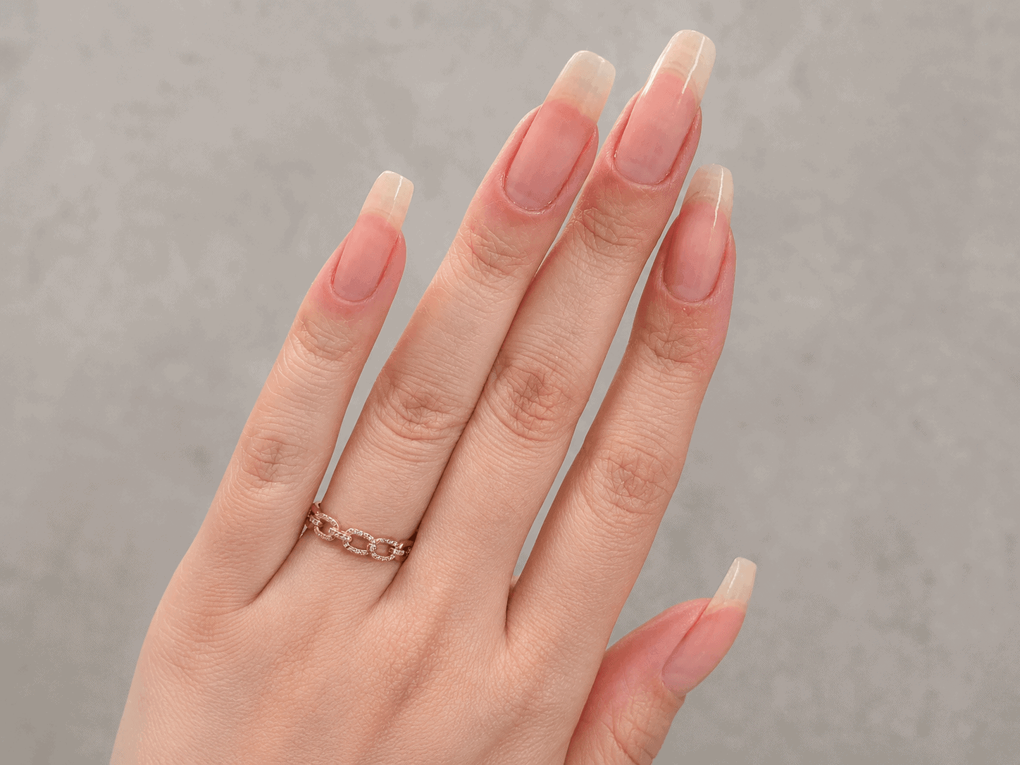 Close-up of long natural nails with a healthy pink and white finish on a hand wearing a rose gold ring