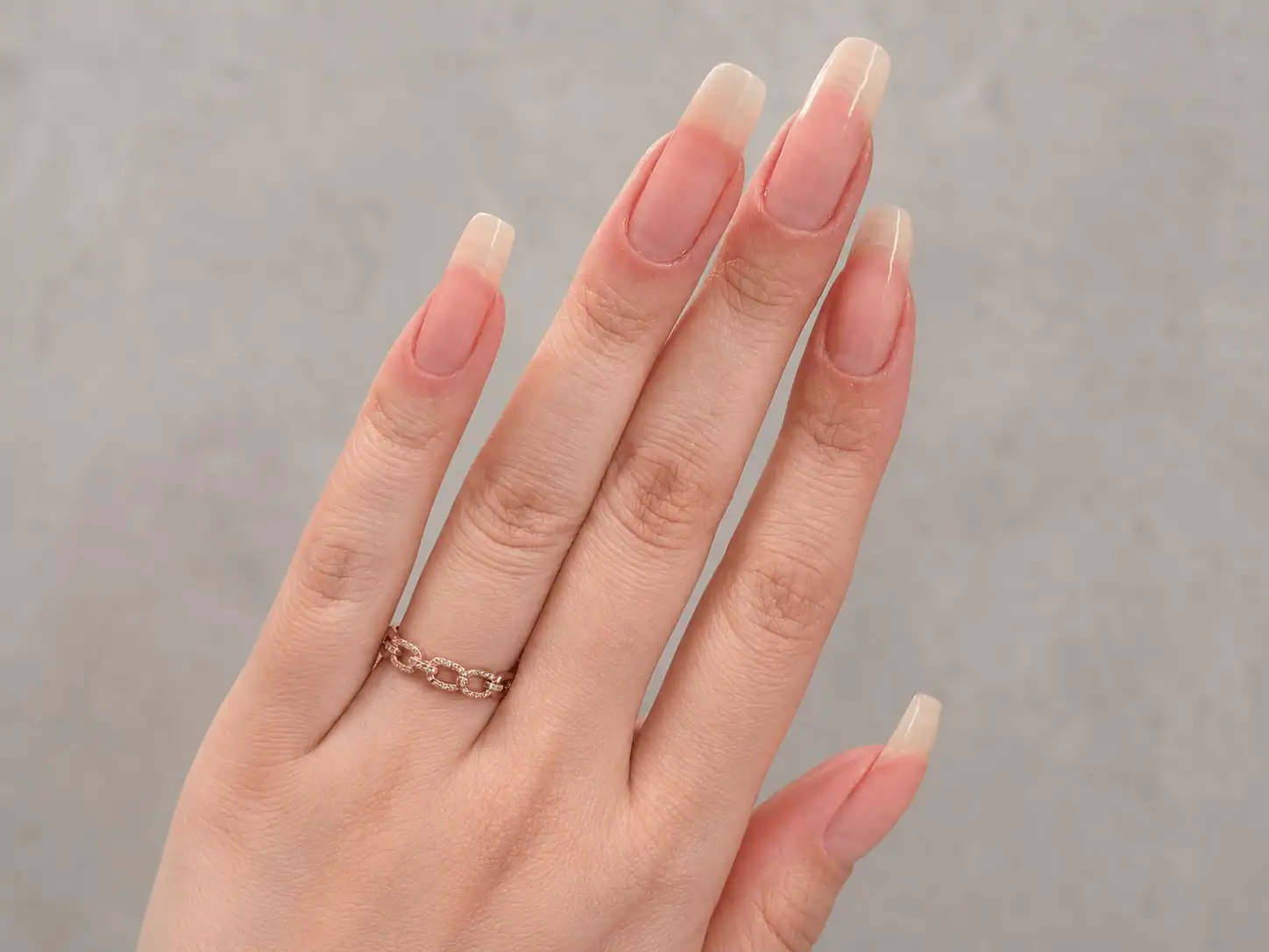 Close-up of long natural nails with a healthy pink and white finish on a hand wearing a rose gold ring