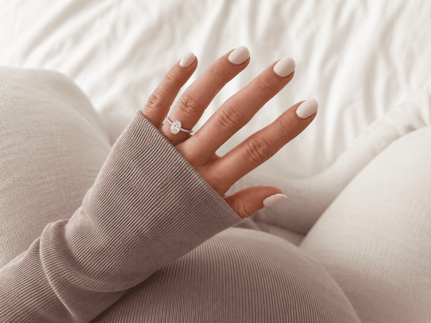 Close-up of short rounded nails with nude gel polish on a hand wearing a diamond engagement ring
